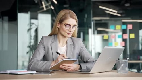 Businesswoman Working at Laptop and Writing Notes