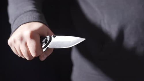 Hand Holding a Silver Knife on Black Background