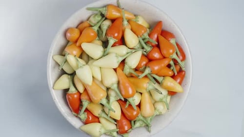 A top view of a white plate filled with assorted mini chili peppers, rotating on a white background.