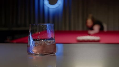 Bartender Carefully Adds Ice to the Cocktail Which is Served in a Neonlit Bar Behind Him a Young