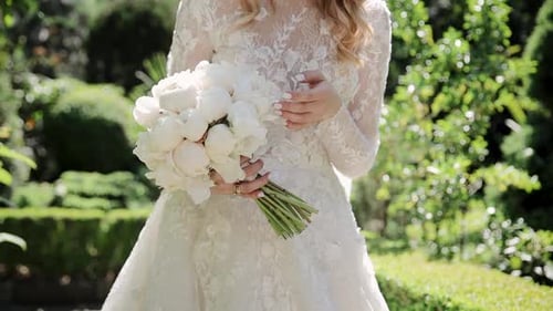 A bride holds wedding flowers bouquet in garden. Charming woman holding leaves and flowers outdoors