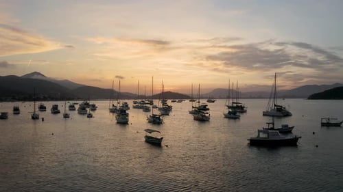 Aerial near water distancing from yachts, boats and sailboats anchored near a brazilian coast at a b
