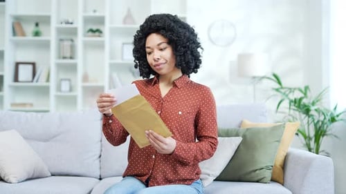 Woman Opens Letter, Reacts with Excitement on Sofa