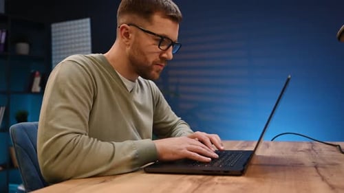 Side view. Male programmer is working indoors by a laptop.
