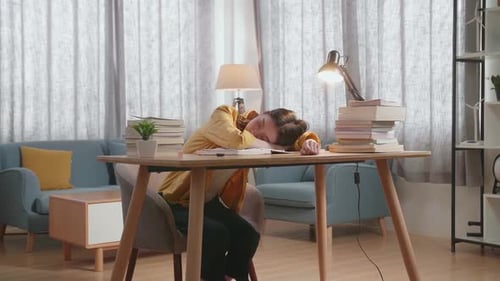 Student Sleeps at Desk with Books and Lamp