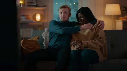 Happy Young Couple Watching Horror Movie on TV while Sitting on a Couch, they got Scared, Girl Cove