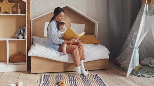 Woman Reading a Book to Baby in Children's Room