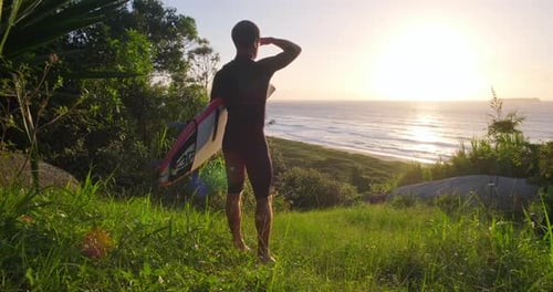 Surfer with board. Surfer in black wetsuit stands on the grass holds the surf board and checks the w