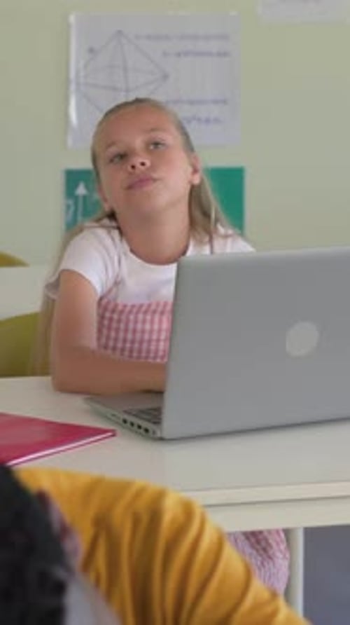 Girl at desk tilting head while camera panning, revealing classmate resting on laptop for lesson