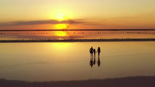 aerial view of happy family walk on sunset by the sea. mom, dad and child daughter having fun on sum