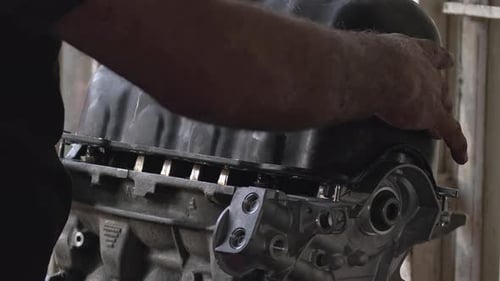 Mechanic At The Repair Shop Installing The Crankcase Cover Of The Car Engine Und At The Bench