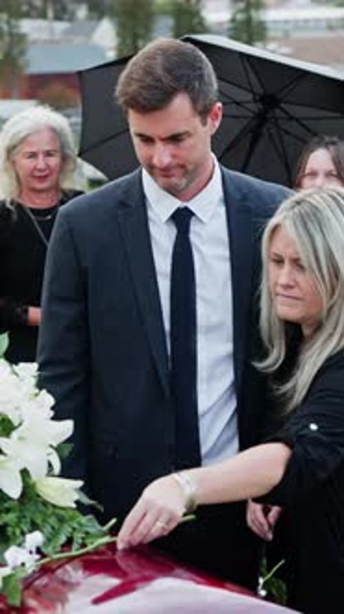Sad, couple and white rose on coffin at funeral for loss, mourning death or honor in cemetery
