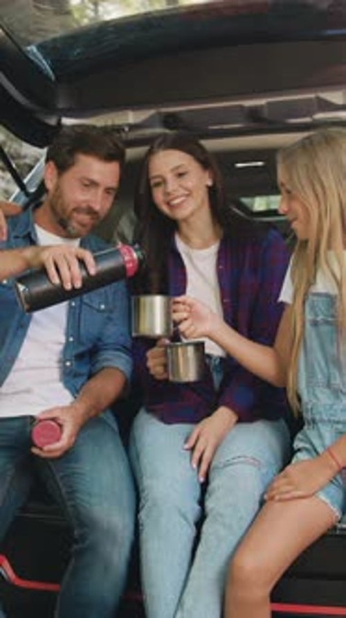 Father Mother and Dougher Son Sitting Inside Car Trunk Near Rocks in Forest and Drinking Tea From
