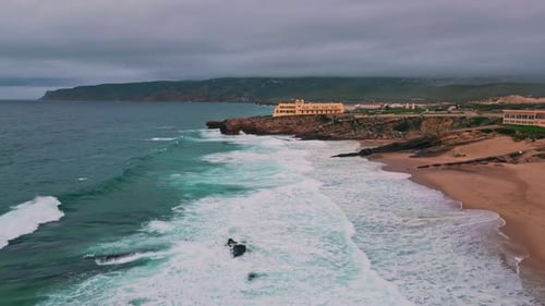 Cliffside Hotel Overlooking Foamy Waves at Serene Beach Dusk Drone View Coast