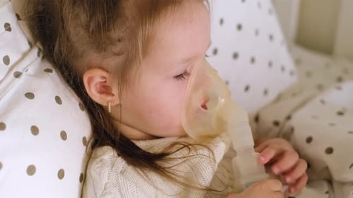 L'enfant qui tousse est allongé dans son lit et respire la vapeur d'un masque d'inhalation