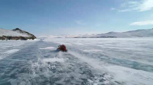 Aerial View on the Hovercraft Driving on Cracked Snowy Ice of Baikal Along the Rocky Cliff Drone