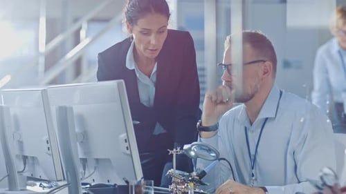 Chefingenieurin spricht mit einem Elektronikspezialisten, erklärt Dinge, er arbeitet am Computer und