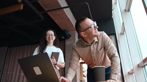 Colleagues look at laptop screen and cheerfully laugh. Happy people working in the office.