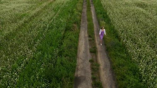 Field of Tranquility Woman Enjoys a Peaceful Walk in a White Flower Field with a Backdrop of Natural
