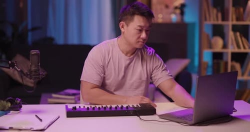 Man Composes Music Using a Laptop and Keyboard