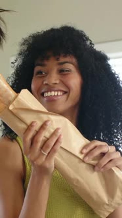 Vidéo verticale : Une femme souriante au sommet vert dans la cuisine prend un bocal de la main gauche pour le tartiner sur une baguette
