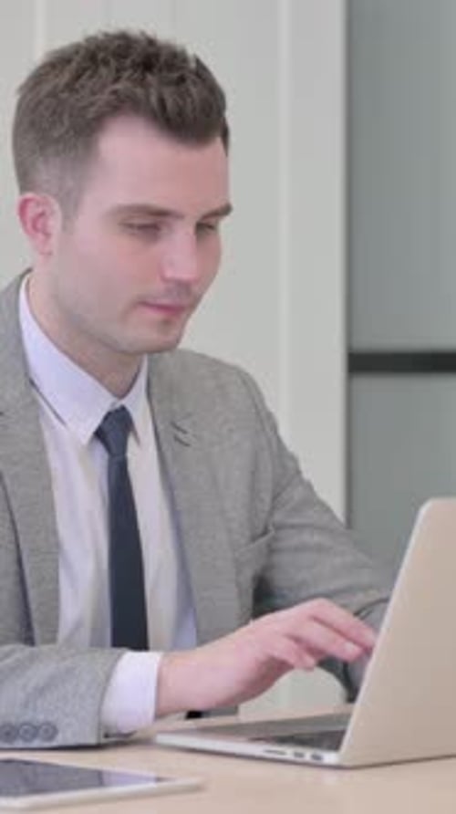 Junger Geschäftsmann verlässt das Büro, nachdem er den Laptop am Abend geschlossen hat, vertikales Video
