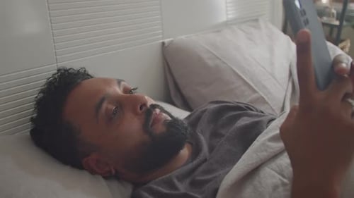 Man Lies in Bed Using Smartphone Indoors