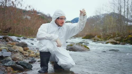 Dissatisfied Biologist in a Protective White Jumpsuit Tests the Water Quality in the River
