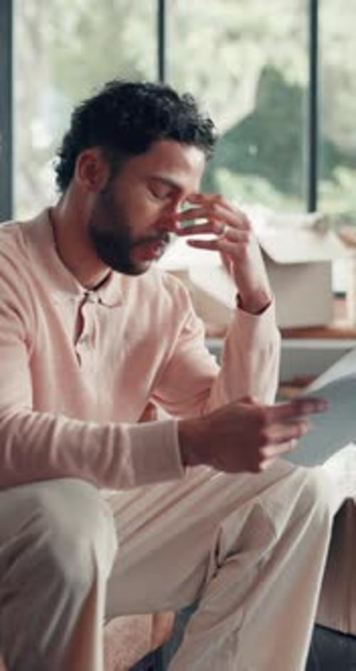 Man Sitting Indoors Looking at Papers with Disappointment