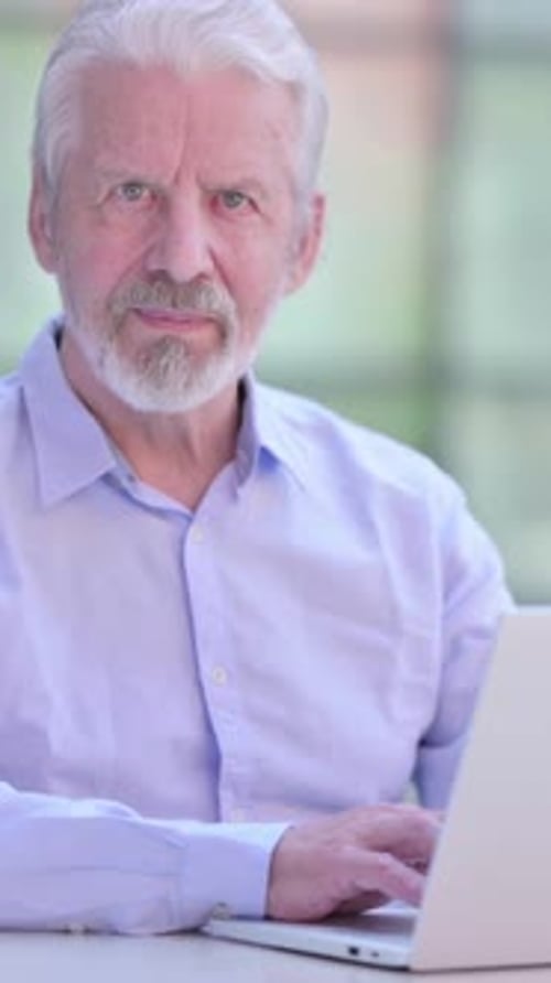 Senior Man Using Laptop Computer Looking at Camera