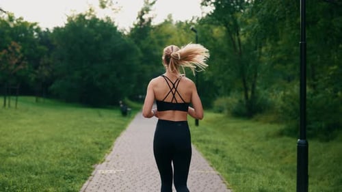 Back View of the Female Athlete is Running in the Park Wearing Black Sportswear