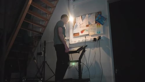 Man Working on Digital Control Panel Under Staircase in Dim Studio Workspace