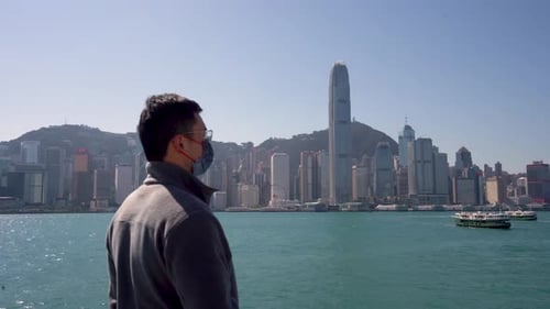 Asian Male Young Adult Wearing Mask Facing City Skyline During COVID 19 Pandemic, Back Facing Camera