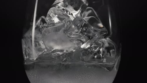 Schmelzende Eiswürfel füllen das Weinglas mit kondensierendem makroschwarzem Hintergrund