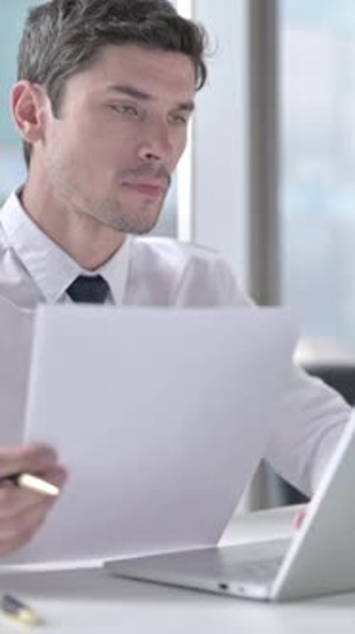 Man Reviews Documents at Desk in Bright Office