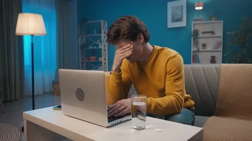 A Man Suffers From an Attack of Headache While Working on a Laptop While Sitting on the Sofa in the