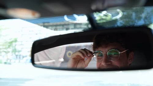 Male Driver Adjusting His Glasses and Looking in the Rear View Mirror While Driving in a Car in the