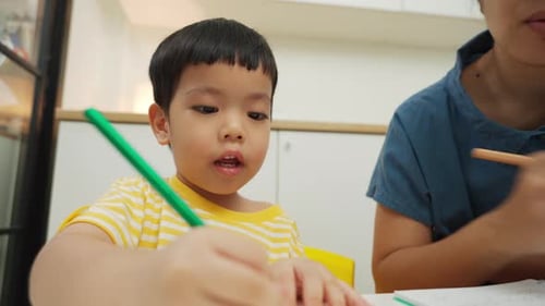 Asian boy student sits with his mother learning drawing in home school