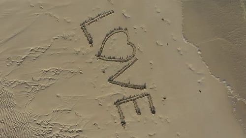 Aerial crazy turning shot of LOVE inscribed in the sand on a beach.