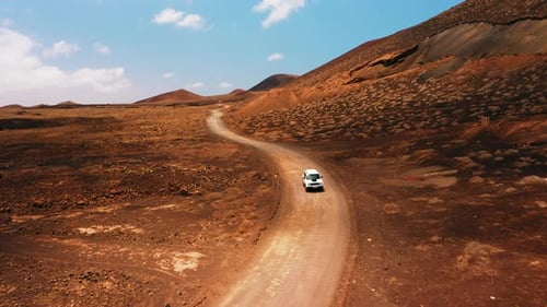 One White SUV Car Driving Alone Travel on Empty Dirt Road Freeway Through Desert Volcanic Landscape