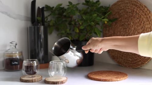 Hand Pours Dark Beverage into Glass in Kitchen