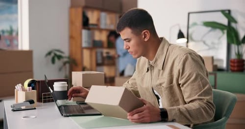 Young Man Works at Laptop, Holds Package