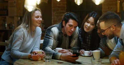 Slow motion of smiling friends having coffee at cafe and having fun with mobile cell phone. Shot i