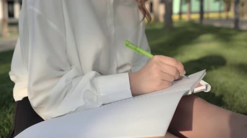 Woman Writing in Notebook in Park on Sunny Day