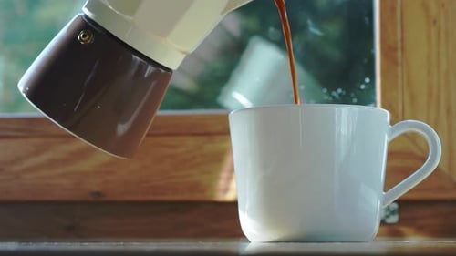 Person Pouring Hot Coffee Drink Into White Cup From Moka Pot. - close up shot