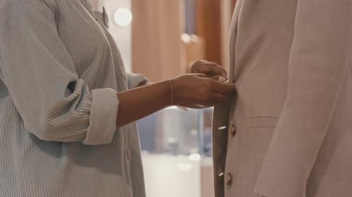 Shop Clerk Buttoning up Coat on Client in Clothes Store