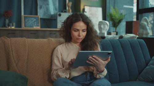 Woman Uses Tablet While Sitting on Sofa Indoors