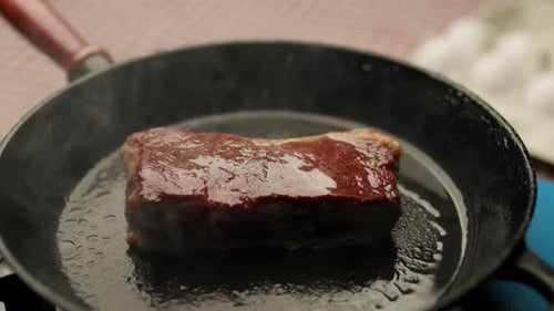 Steak sizzling and cooking in hot cast iron pan