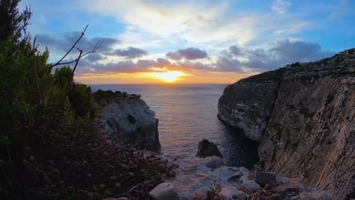 Golden sunset captured in a time-lapse, descending over serene rocky cliffs by the sea.