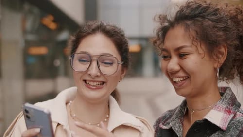 Two Friends Smiling at Cellphone in the City
